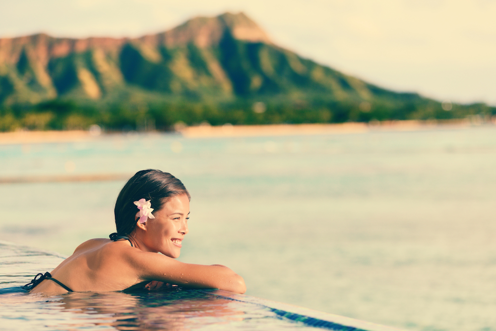 Woman in an infiniti pool in Hawaii with mountain and ocean in background