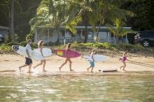 family of 5 each with surfboards walking along beach