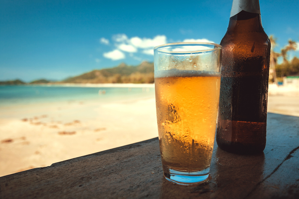 beer glass and bottle in foreground with blurred beach scene in background
