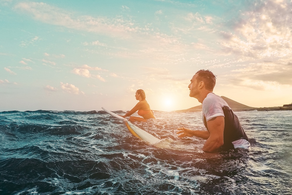 couple surfing at sunset